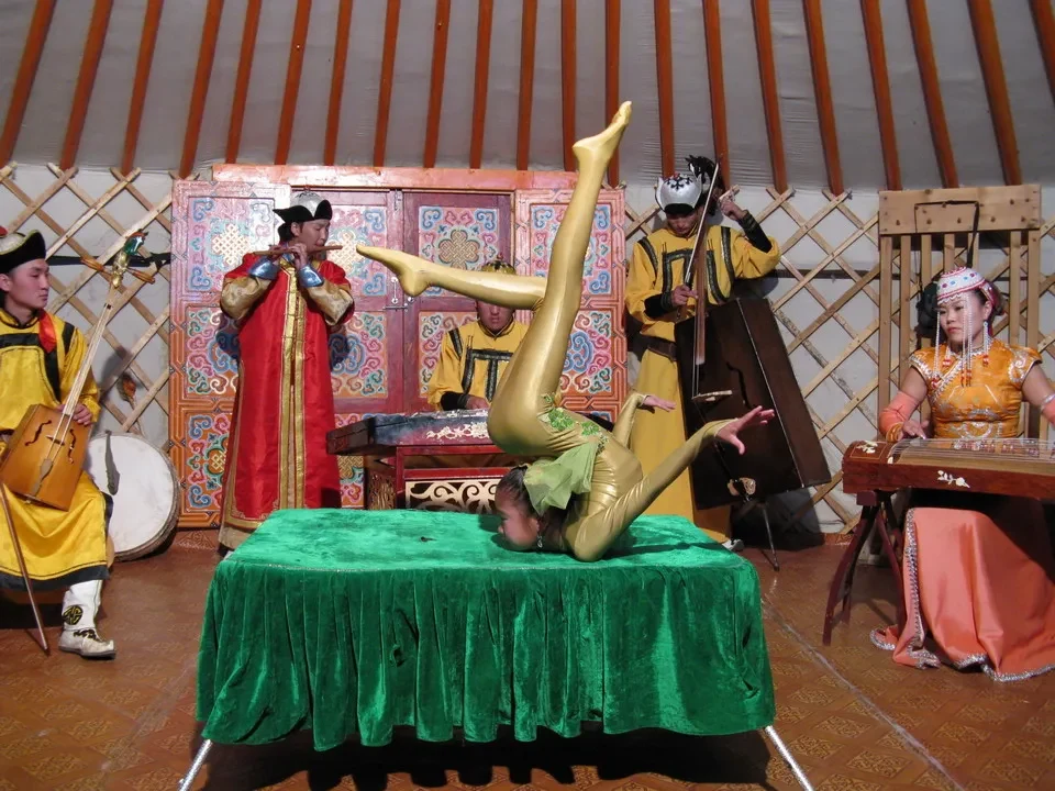 Una performance tradizionale mongola con costumi colorati e una figura centrale dorata in posa.