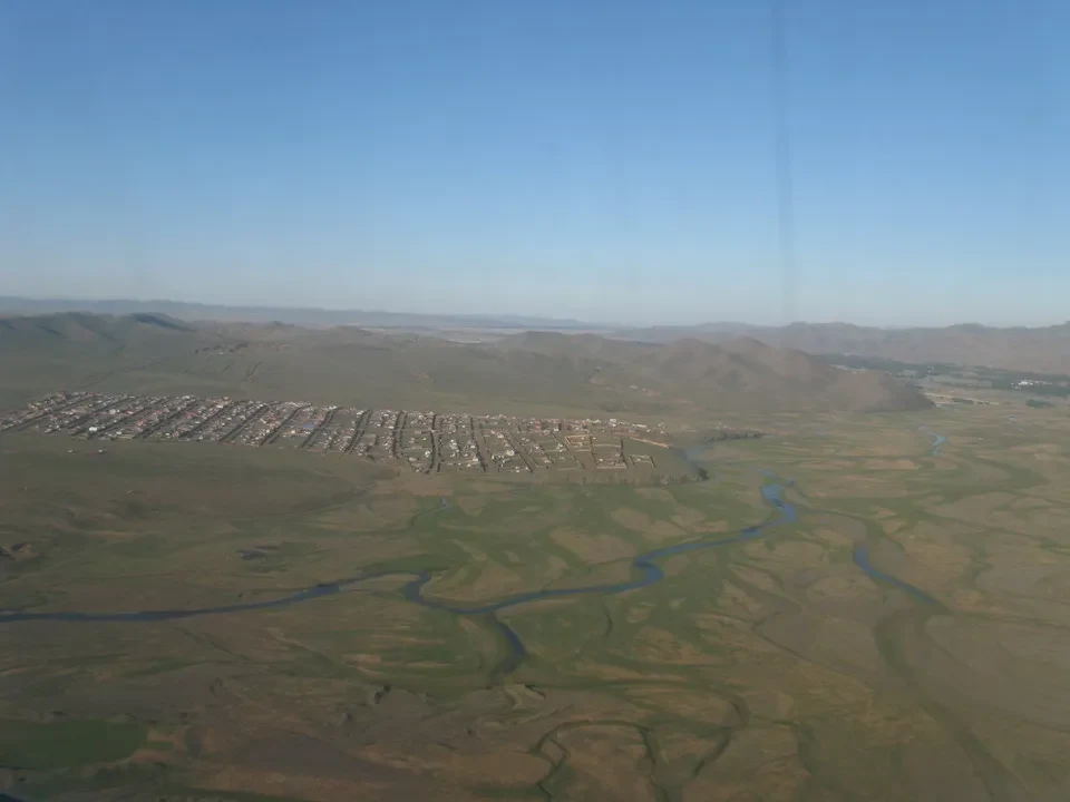 Paesaggio vasto della Mongolia con un fiume serpente che attraversa la pianura.