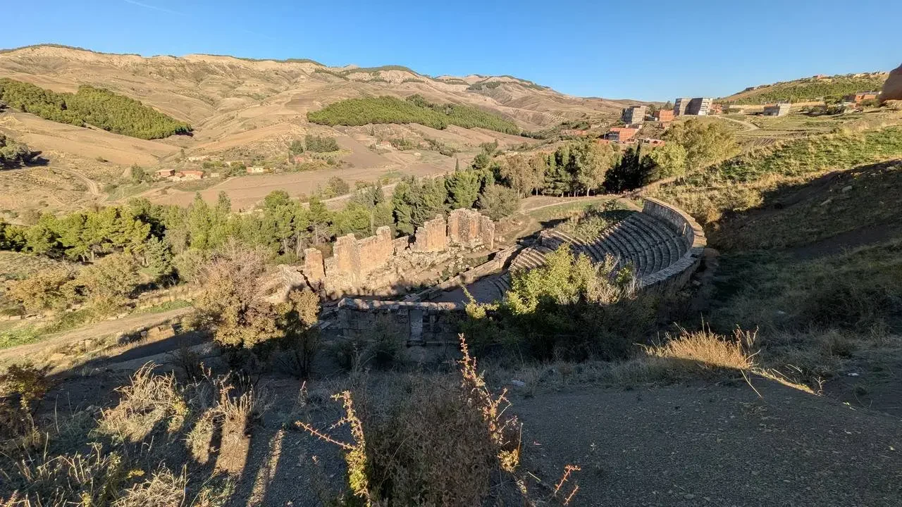 Rovine di un antico teatro romano si stagliano su un paesaggio collinare in Algeria.