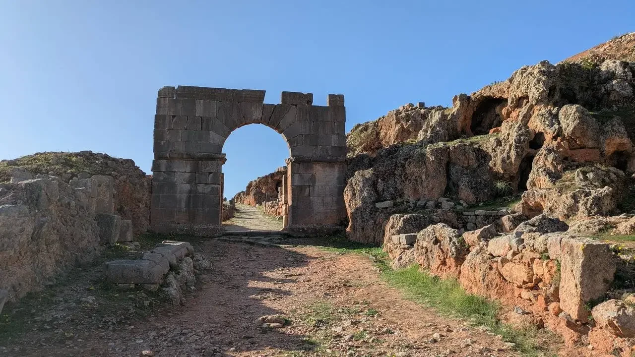 Rovine romane visibili attraverso un arco in pietra in un paesaggio arido.