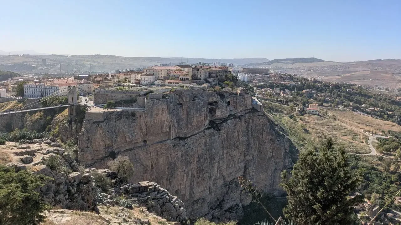 Paesaggio roccioso e collinare con insediamenti sotto una scogliera imponente.