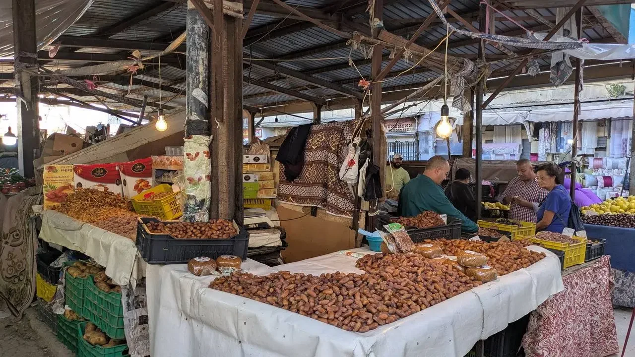 Una bancarella all'aperto espone diverse merci, inclusi frutta secca e prodotti alimentari in un mercato algerino.
