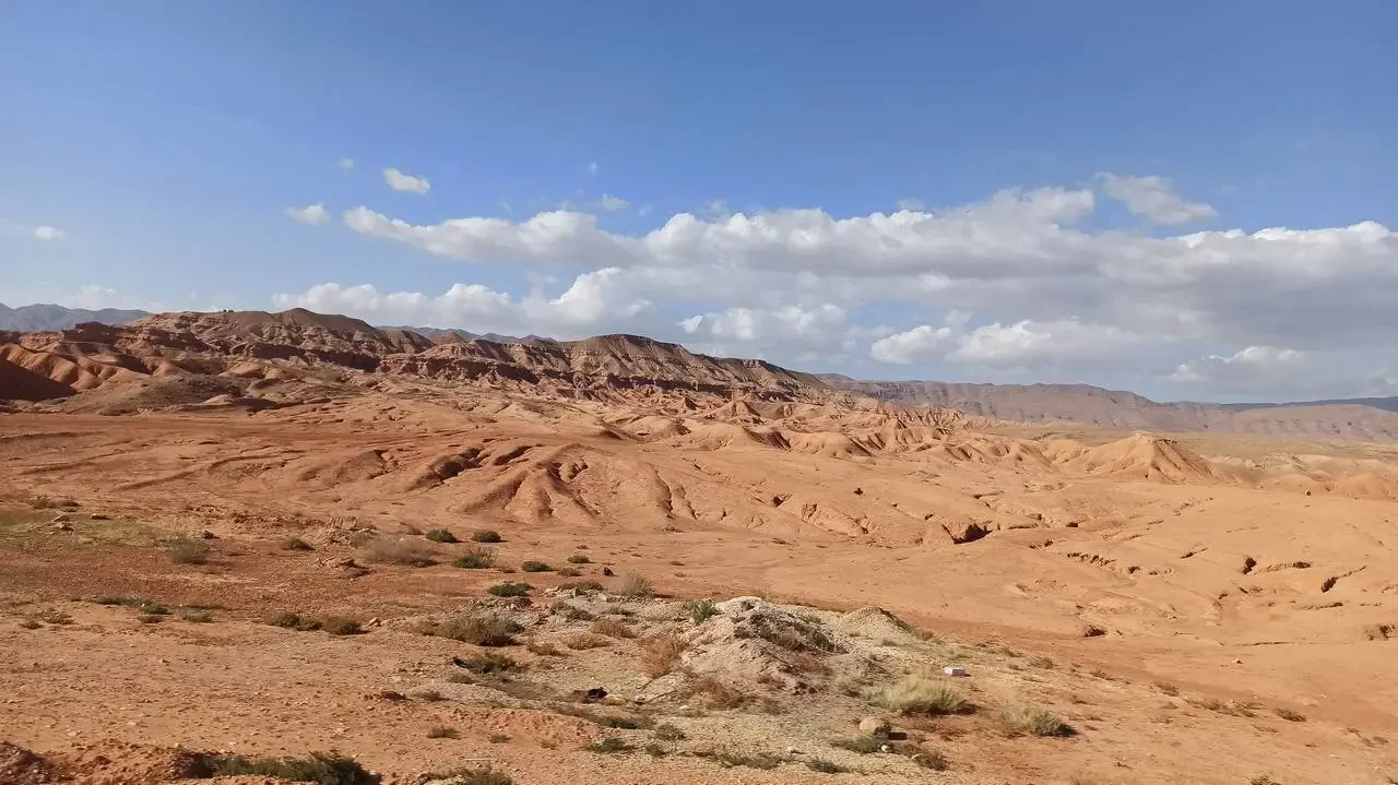 Paesaggio desertico in Algeria con colline aride sotto un cielo azzurro e nuvoloso.
