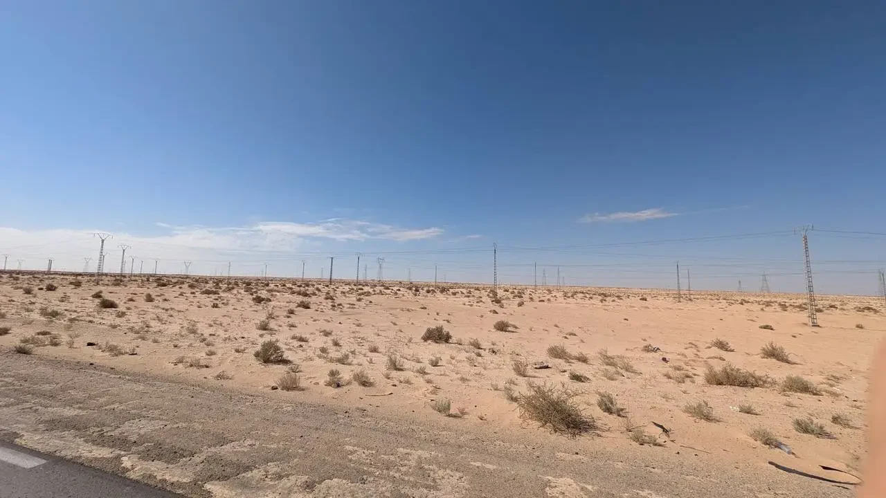 Paesaggio arido del deserto con linee elettriche che si estendono all'orizzonte sotto un cielo azzurro.