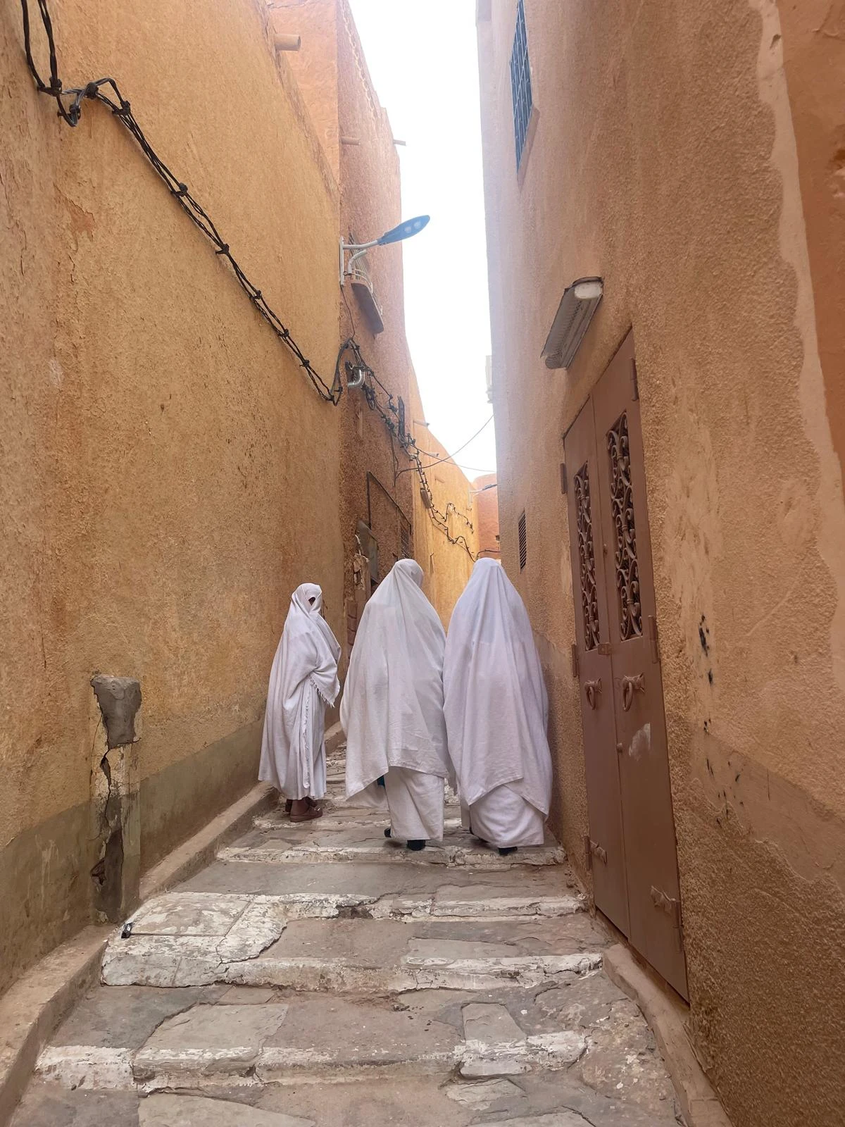 Due uomini vestiti di bianco camminano lungo una stretta via in un quartiere nordafricano.