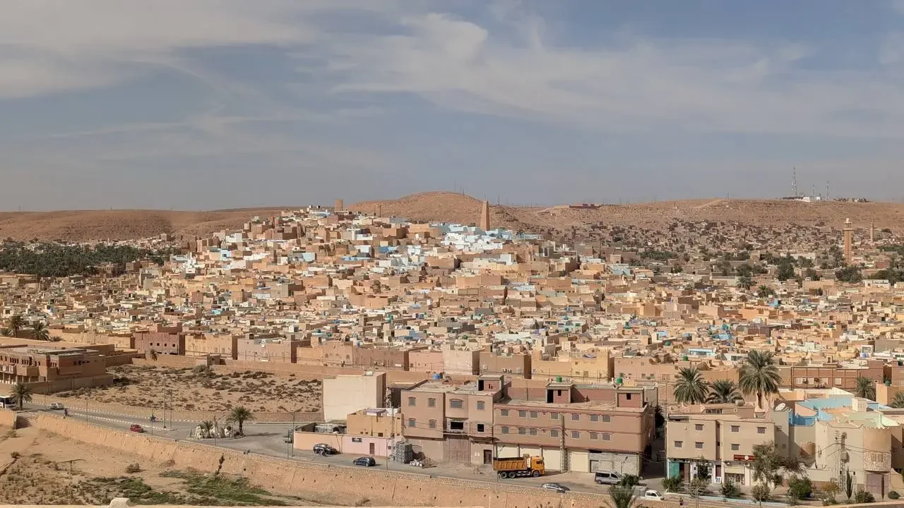 Vista aerea di una città arida in Algeria con case basse e strutture in terra cotta sotto un cielo chiaro.