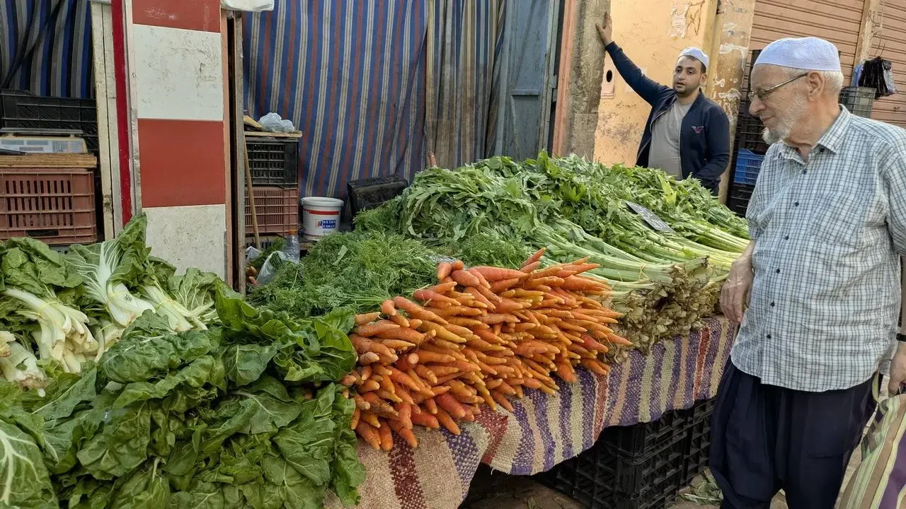Un uomo mostra una grande quantità di verdure fresche in un mercato algerino.
