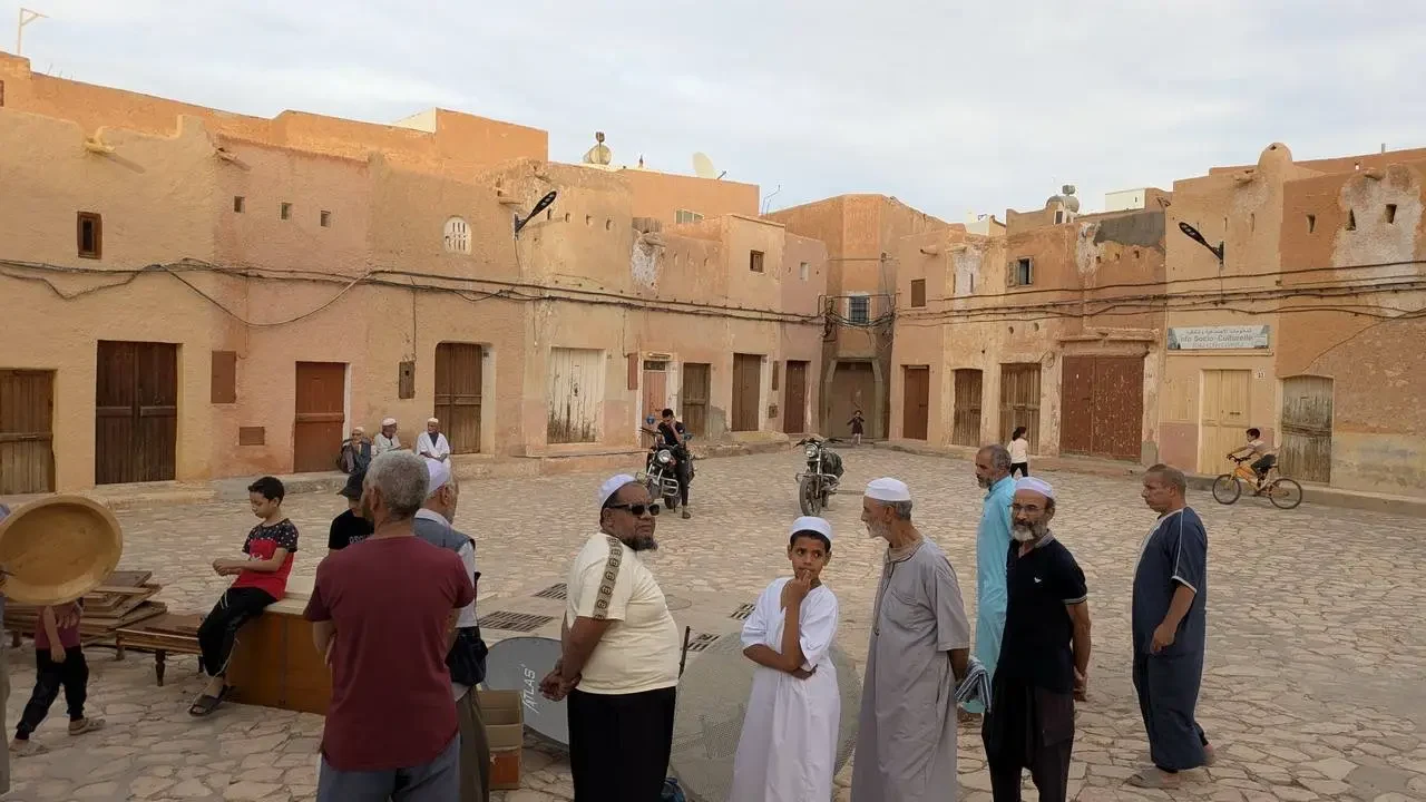 Uomini in abiti tradizionali si radunano in una piazza di un villaggio tradizionale in pietra in Algeria.