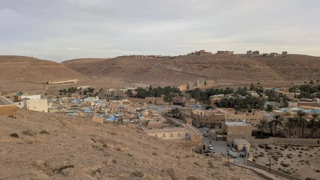 Paesaggio urbano e desertico in Algeria con edifici sparsi sotto un cielo chiaro.