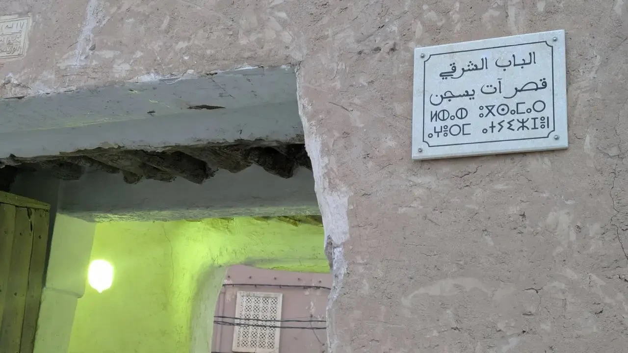 Muro esterno rustico di un edificio con un cartello bianco in arabo appeso.