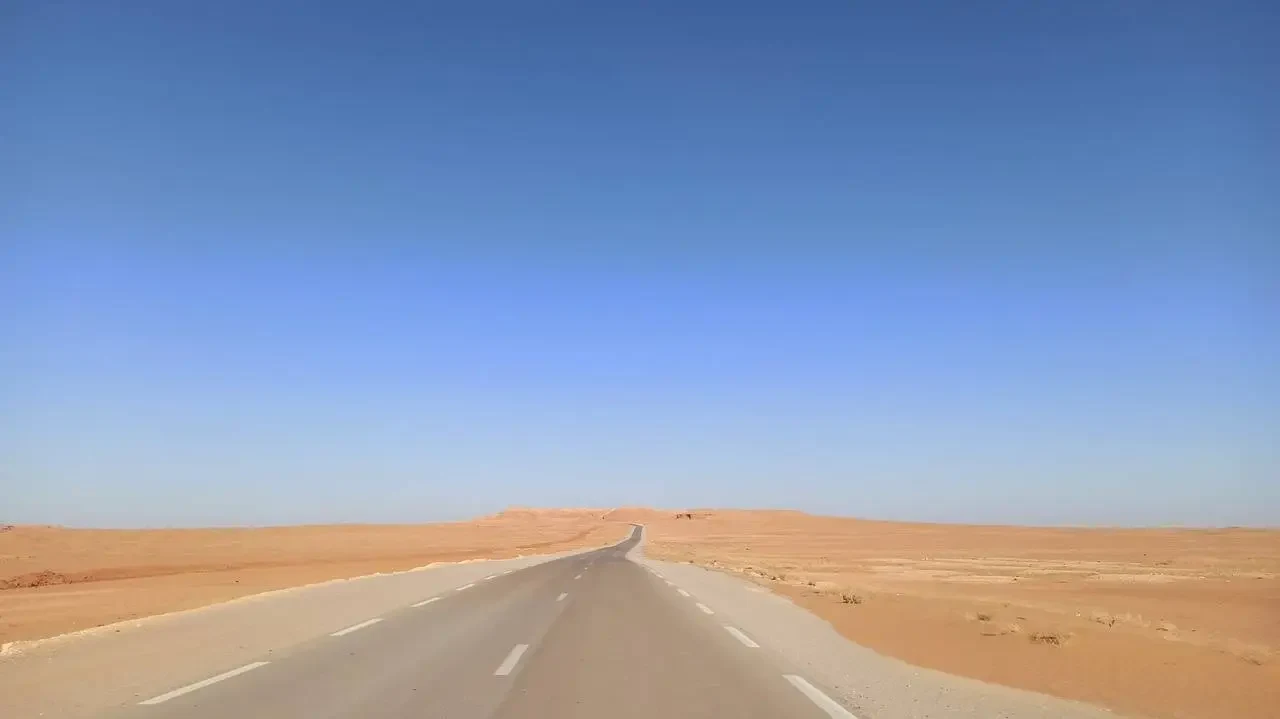 Una strada asfaltata attraversa un vasto paesaggio desertico in Algeria.