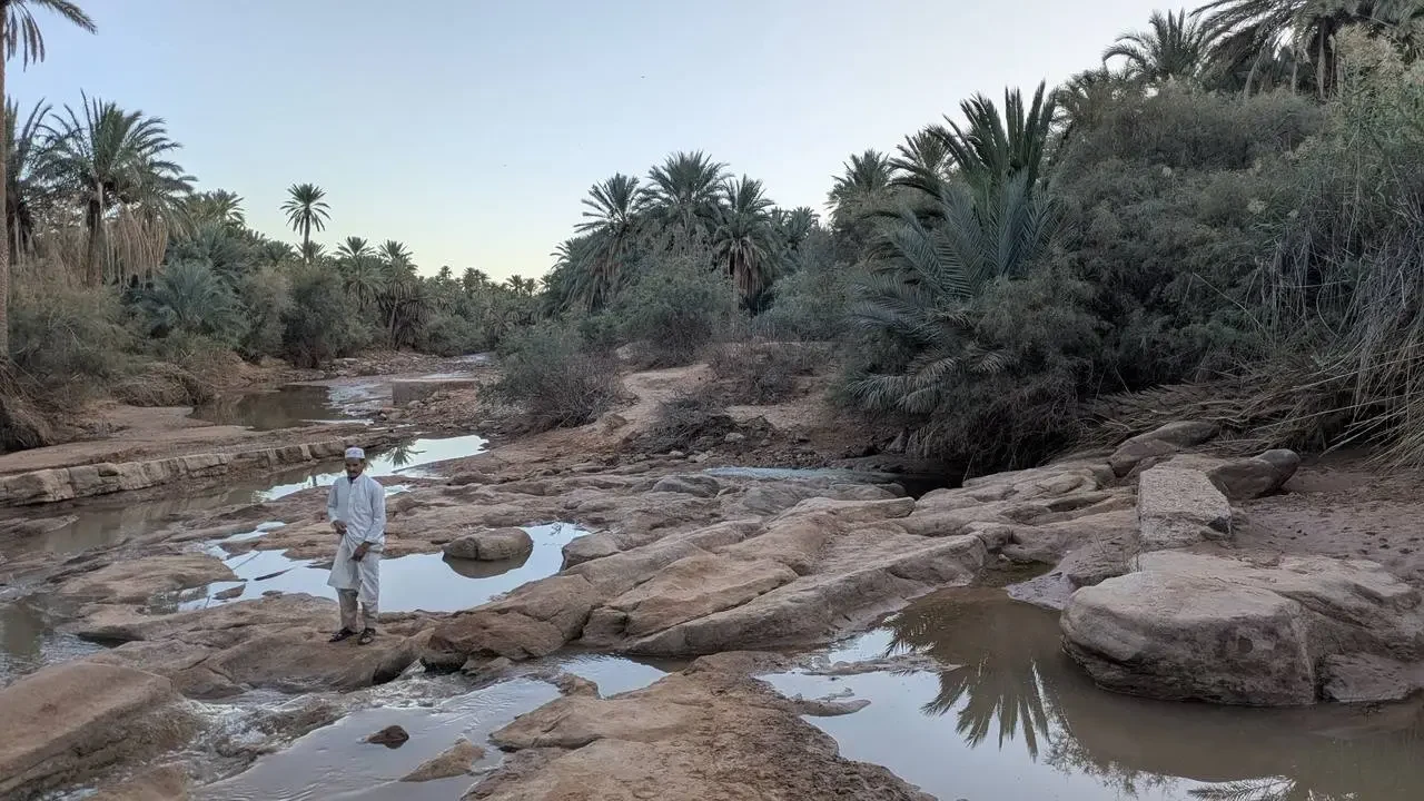 Un uomo si trova su rocce lungo un letto di fiume secco e roccioso in un paesaggio arido.
