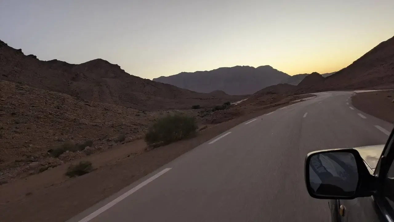Una strada asfaltata serpeggia attraverso un paesaggio montuoso e arido all'alba o al tramonto.