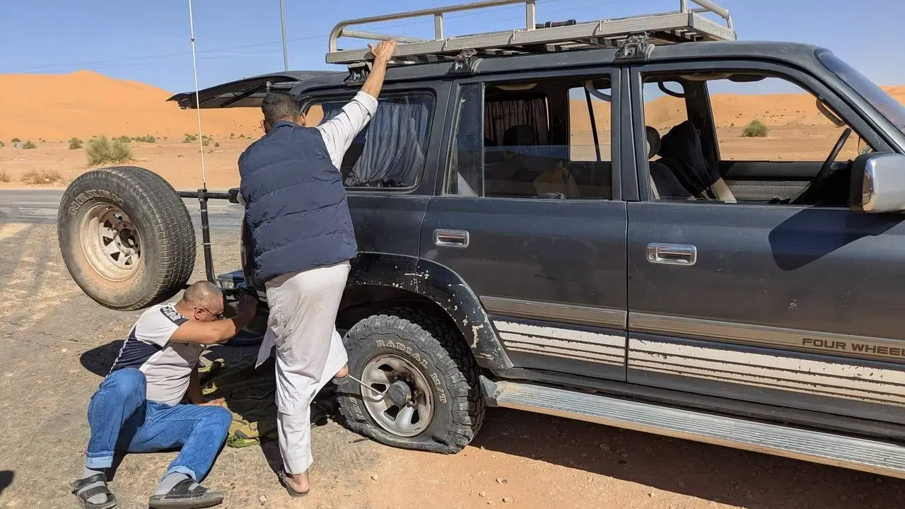Due uomini lavorano insieme sul tetto di un fuoristrada nel deserto algerino.
