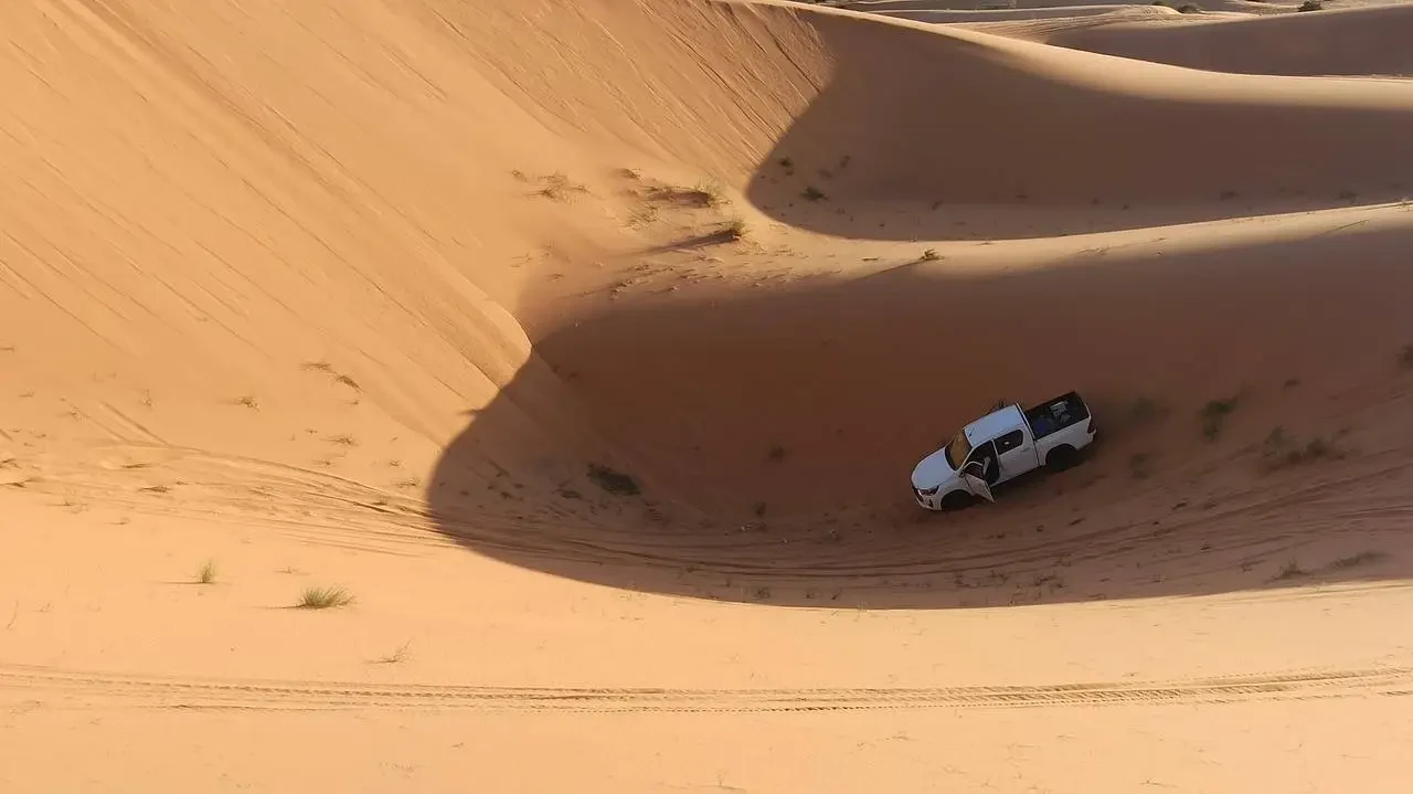 Un veicolo bianco attraversa dune di sabbia dorata in un paesaggio desertico.