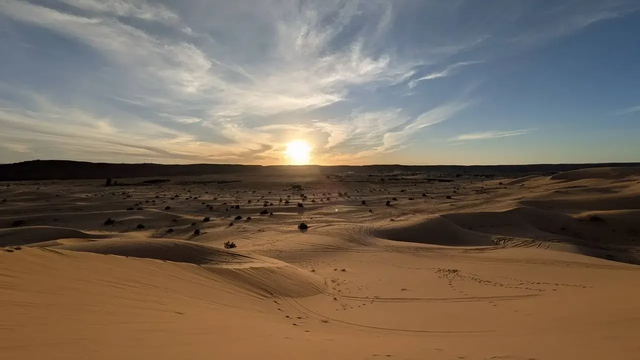 Vaste dune di sabbia si estendono attraverso un paesaggio desertico al tramonto.