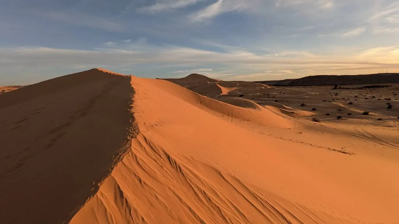Dune di sabbia arancione che si estendono sotto un cielo chiaro.