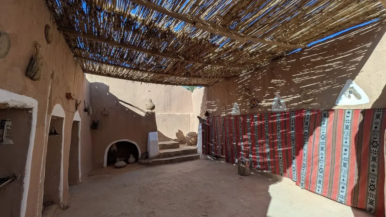 Interno tradizionale di un cortile algerino con tetto di paglia e decorazioni tessili.