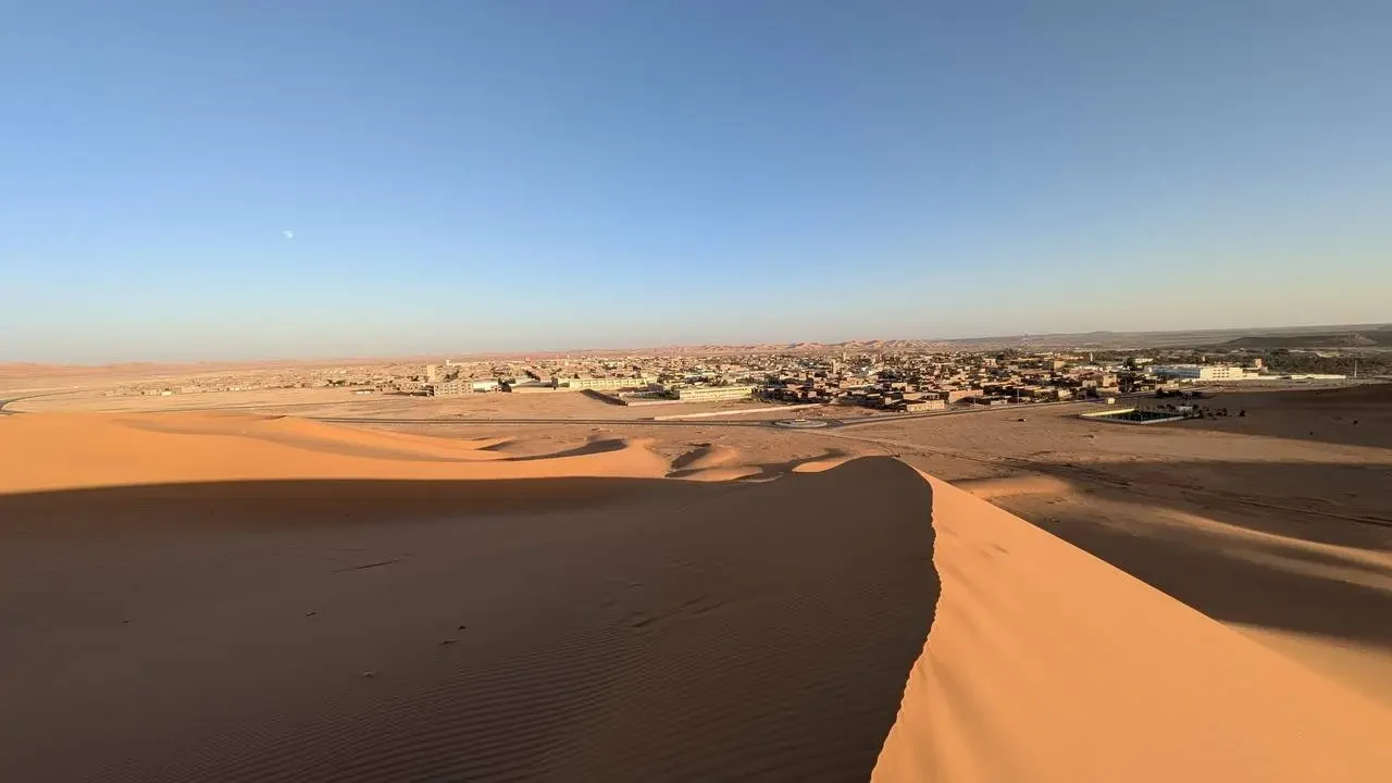 Paesaggio desertico al tramonto in Algeria con un paesaggio urbano in lontananza.
