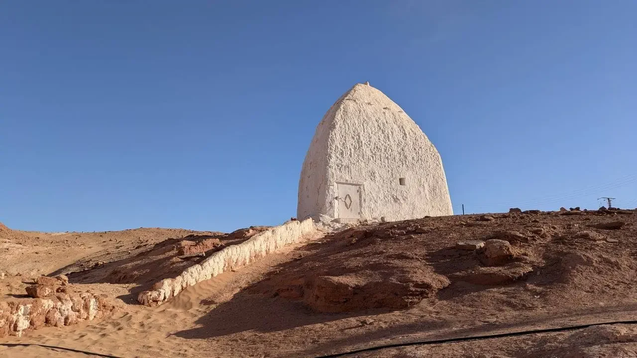 Una piccola struttura a cupola bianca si erge su un terreno collinare arido.