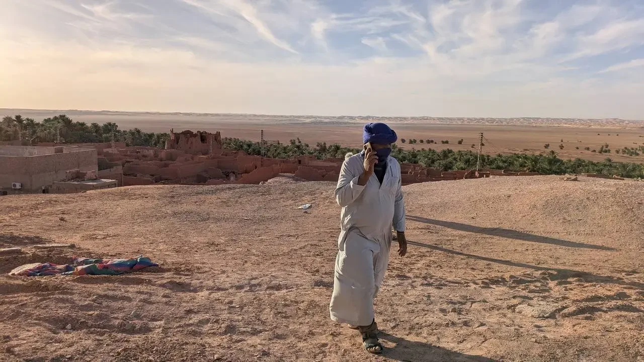 Un uomo cammina attraverso un paesaggio arido in Algeria al tramonto.