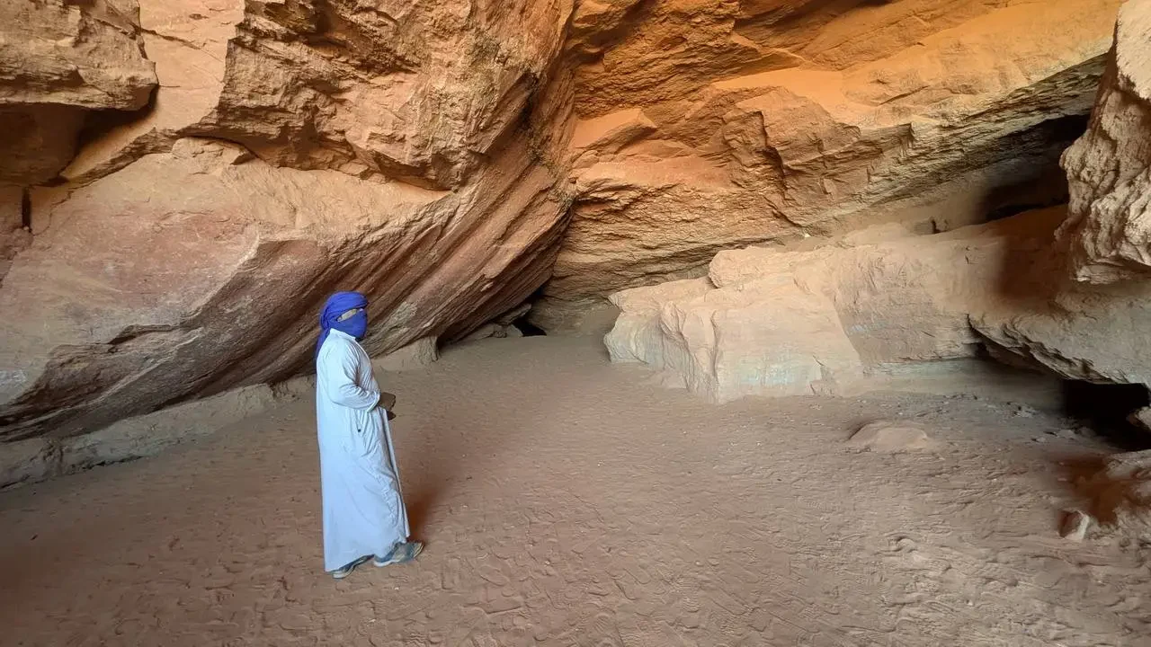 Una persona in abito bianco si trova all'interno di una grotta rocciosa in Algeria.