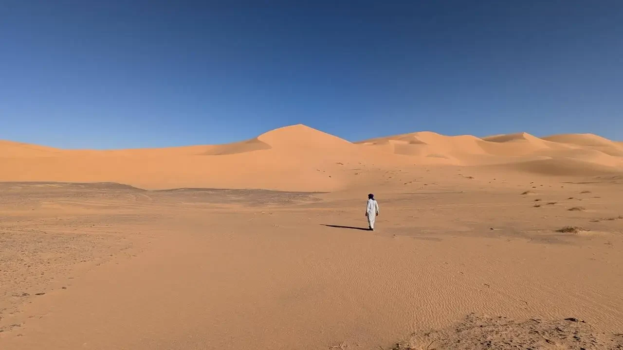 Una persona cammina attraverso le dune del deserto.