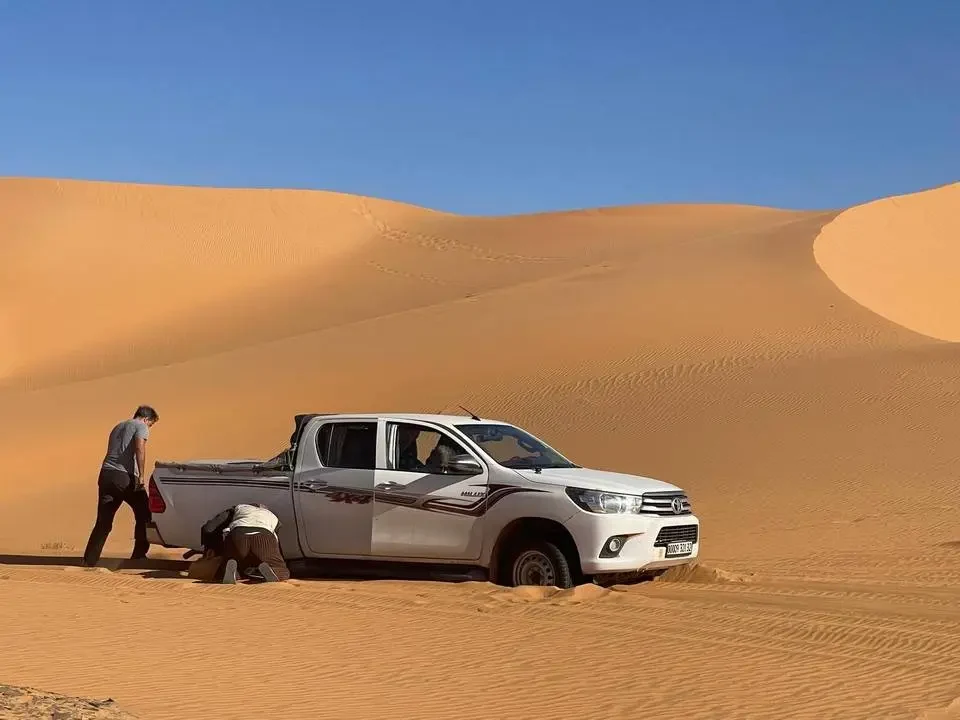 Un pick-up truck is parked in the sand dunes of the Algerian desert.