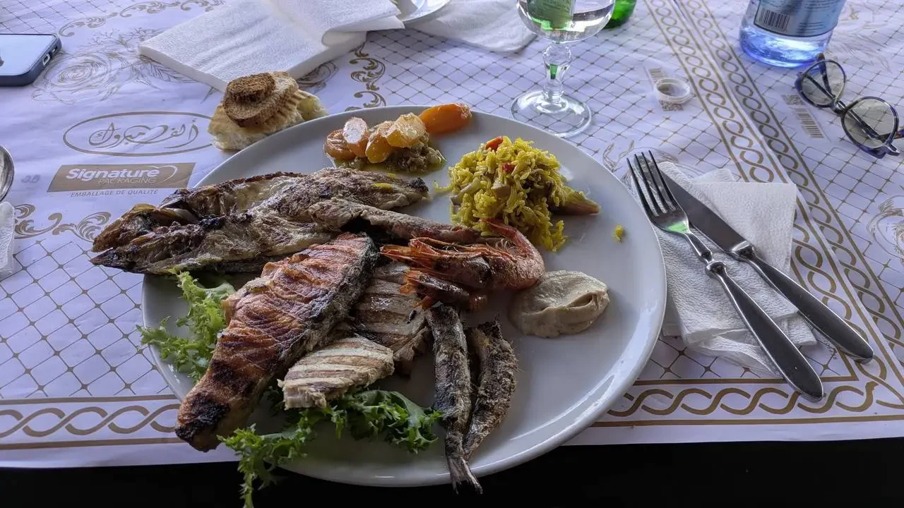 Un piatto di pesce e carne alla griglia con contorni in un contesto algerino.