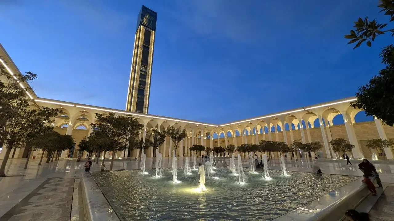 Vista notturna del Djamaa el-Kebir ad Algeri con fontane e un edificio moderno in primo piano.