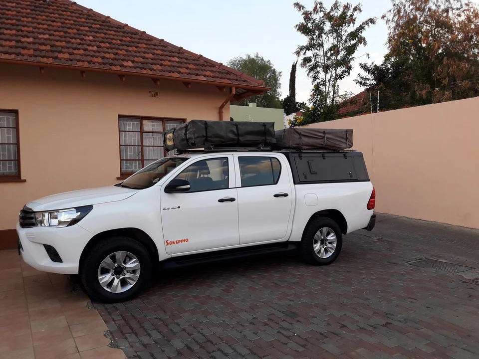 Un Toyota Hilux bianco parcheggiato davanti a una casa in un ambiente secco.