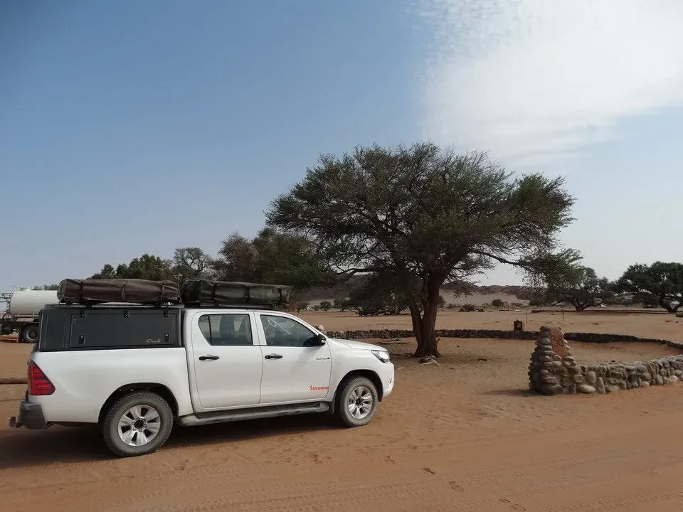 Un veicolo bianco si ferma su un terreno sabbioso con alberi isolati in Namibia, Botswana o Zimbabwe.