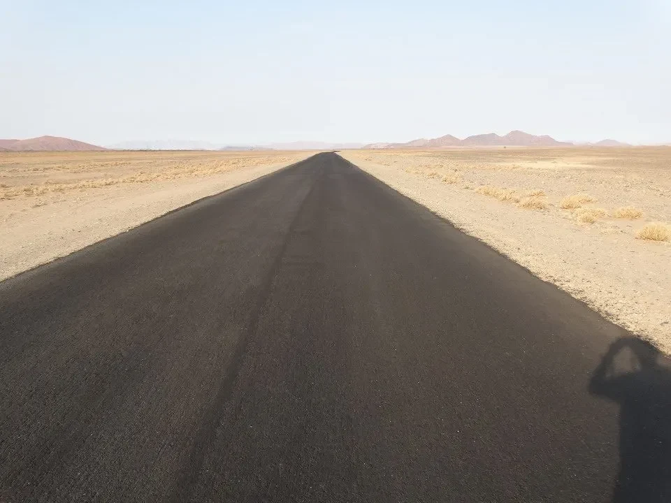 Una strada asfaltata si estende attraverso un paesaggio arido del Namibiano, Botswana e Zimbabwe.