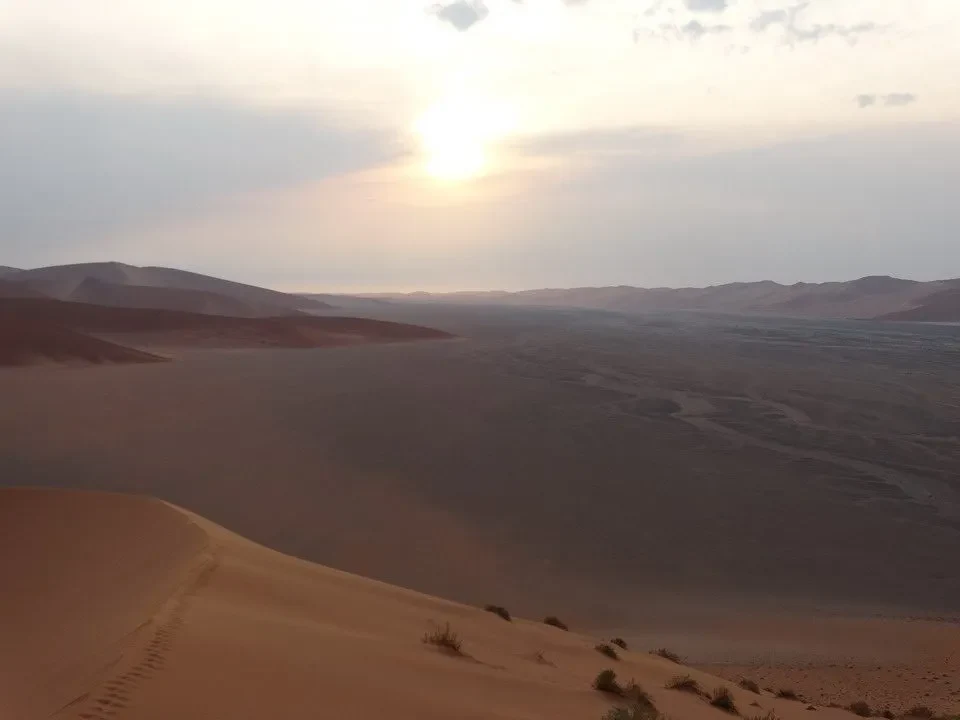 Dune di sabbia ondulate sotto il sole basso al tramonto nel deserto africano.