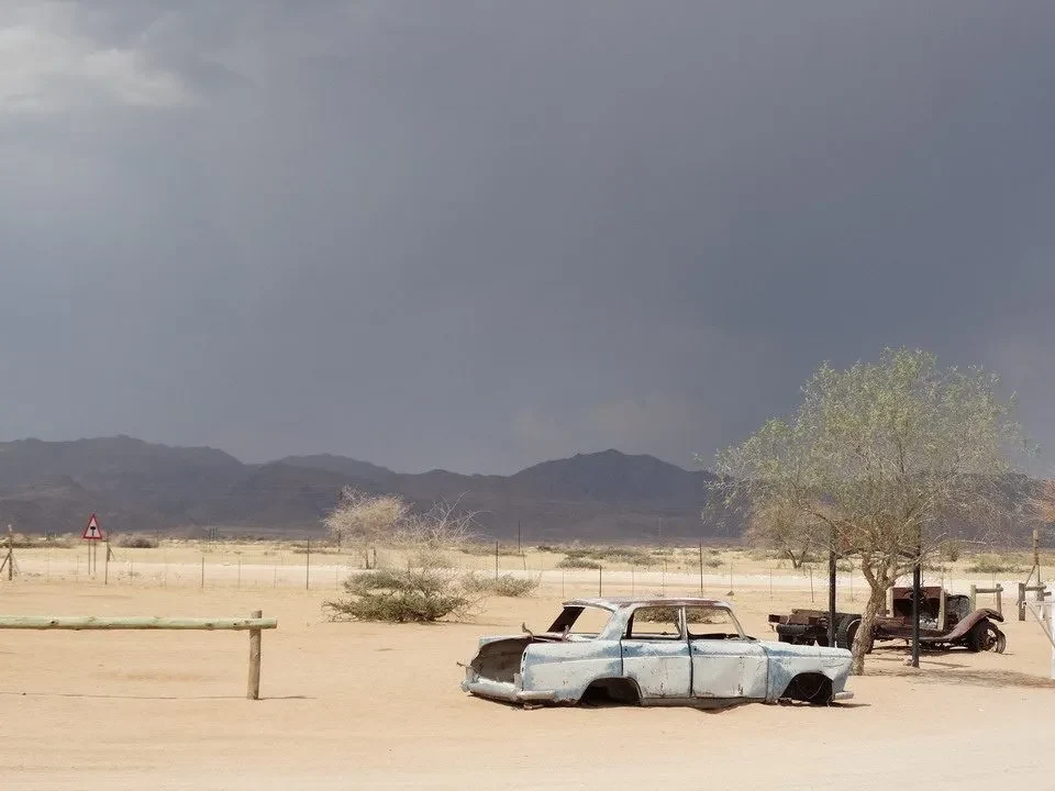 Un'auto abbandonata è parcheggiata in un paesaggio arido sotto un cielo temporalesco.