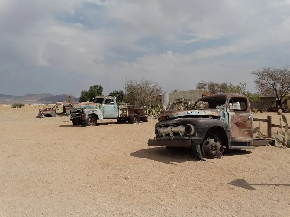 Un vecchio camion arrugginito è parcheggiato su un terreno sabbioso in una savana africana.