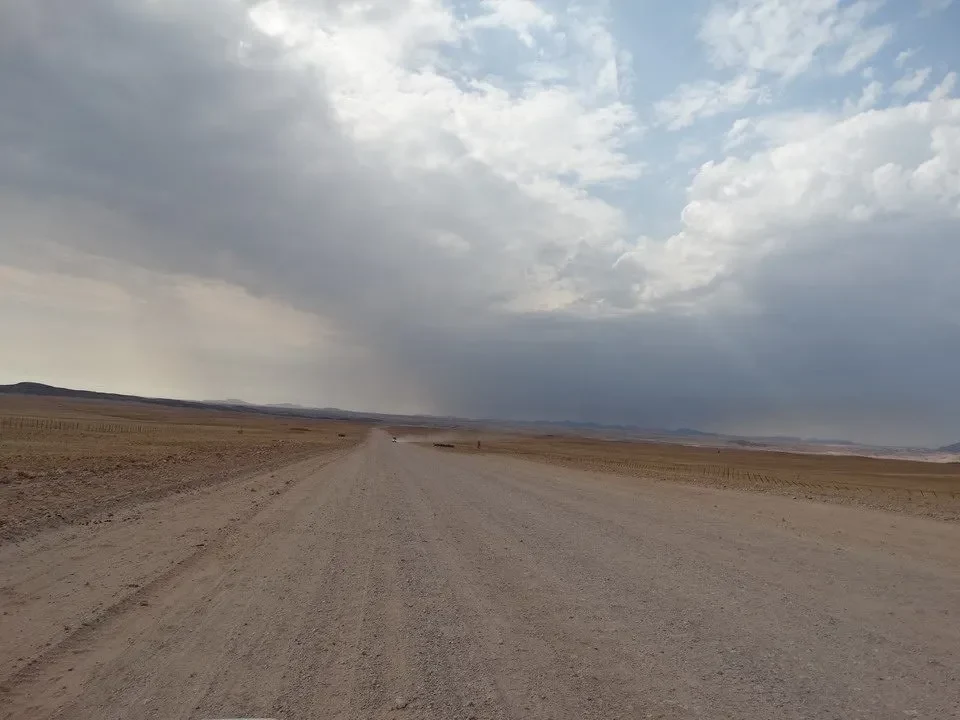 A strada sterrata attraversa un paesaggio arido sotto un cielo nuvoloso.