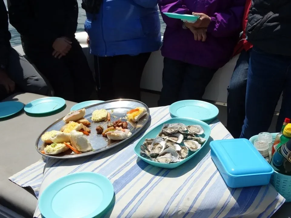 Un gruppo di persone condivide un pasto all'aperto con cibo servito su piatti metallici e piatti colorati.
