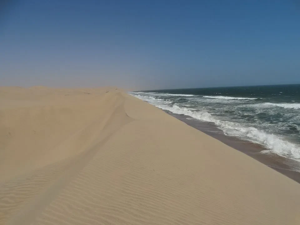 Una spiaggia sabbiosa si estende verso l'orizzonte con onde che si infrangono sulla riva.