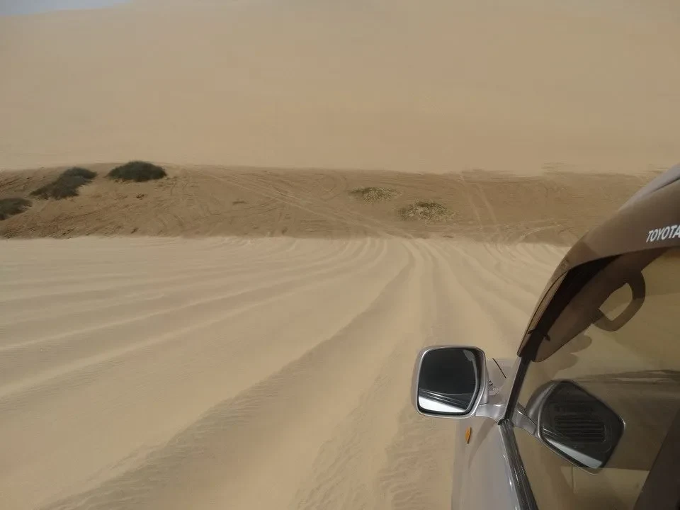 Un veicolo attraversa dune di sabbia in un paesaggio arido.