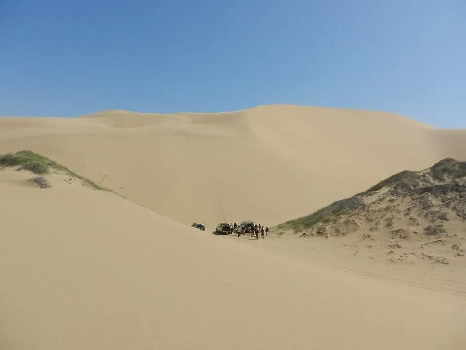 Dune sabbioso con alcune persone in lontananza sotto un cielo azzurro.