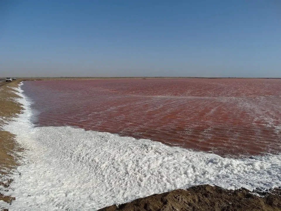 Onde d'acqua rosse incontrano la riva sotto un cielo limpido.
