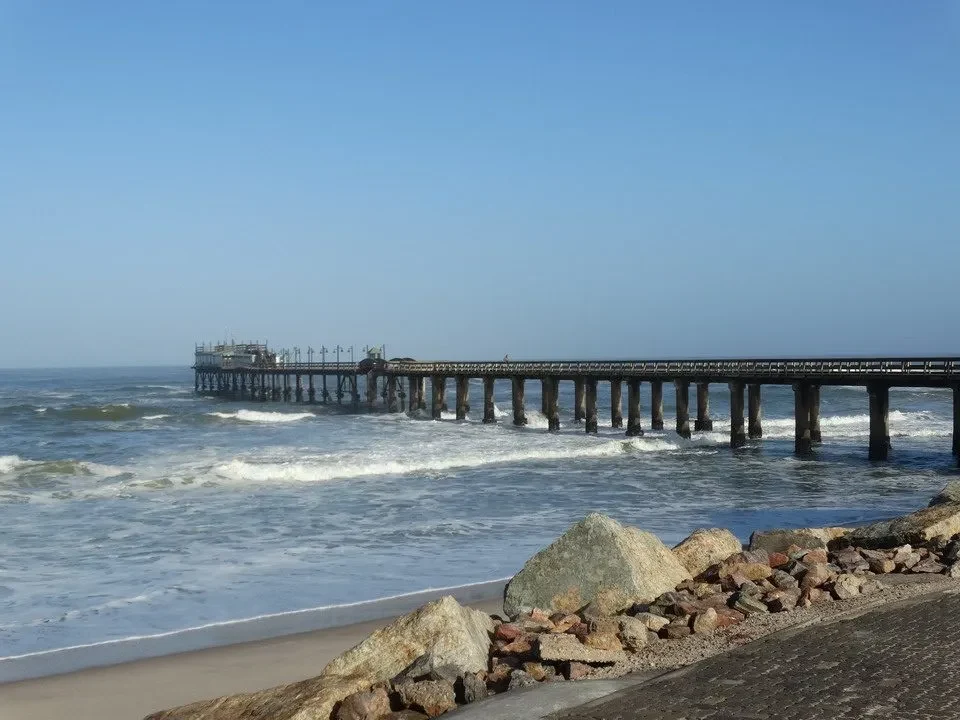 Una passerella di legno si estende sopra le onde del mare in una costa africana.