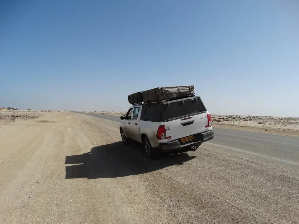 Un veicolo bianco percorre una strada sterrata in un paesaggio arido africano.