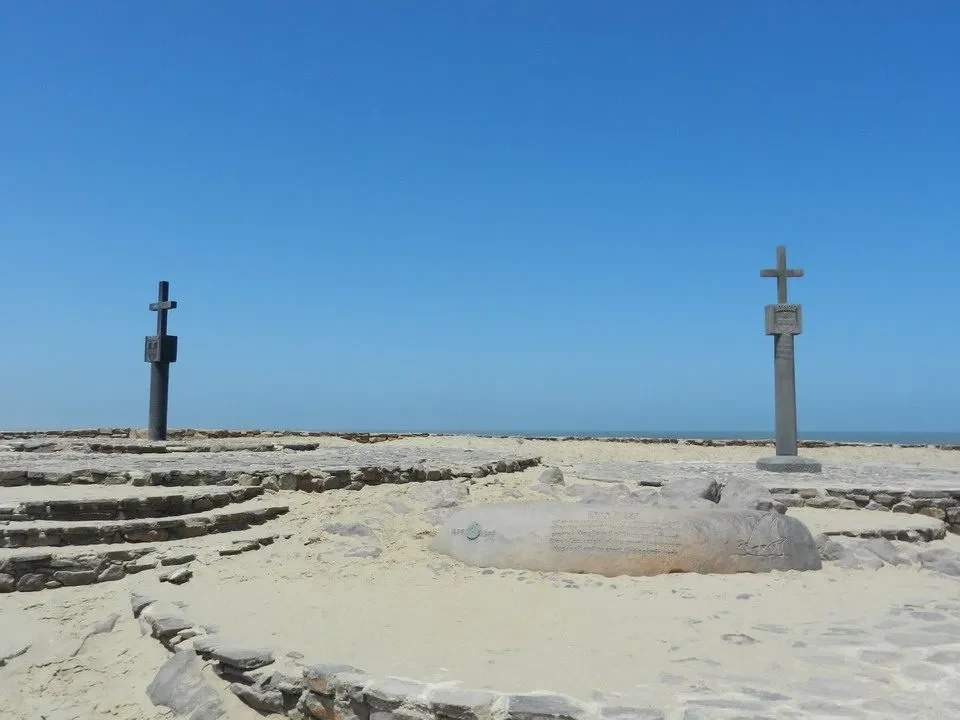 Croci di pietra e una grande pietra giacciono sulla spiaggia sotto il cielo blu.