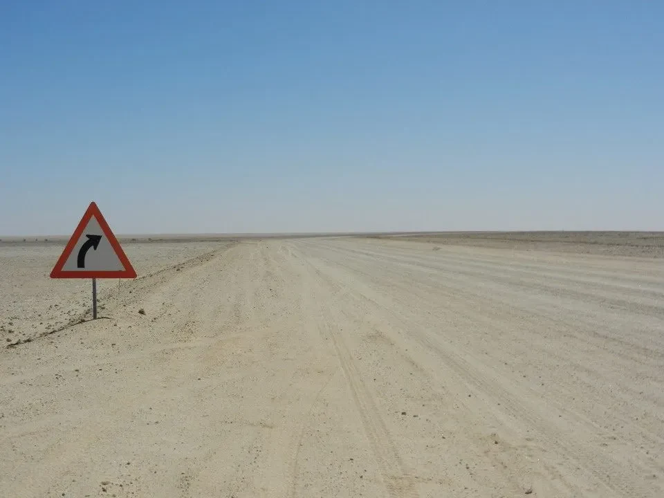 Segnale stradale di pericolo che indica una curva a sinistra in un paesaggio deserto.