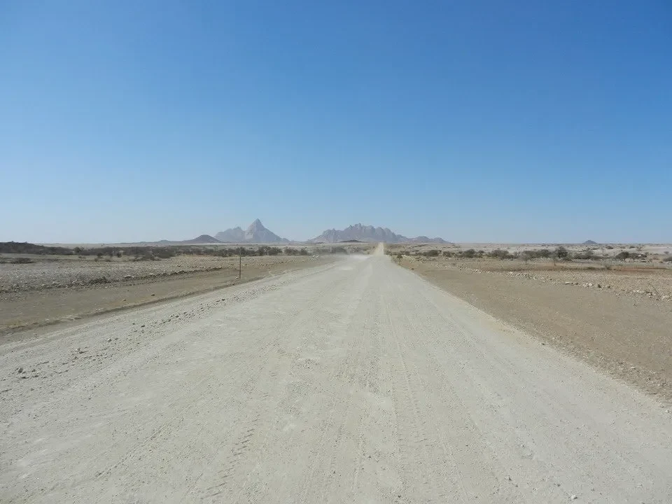 Una strada sterrata si estende attraverso un paesaggio arido del Namib o Botswana.