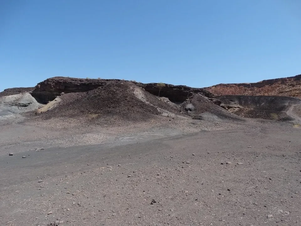 Un paesaggio arido con colline scure sotto un cielo azzurro.