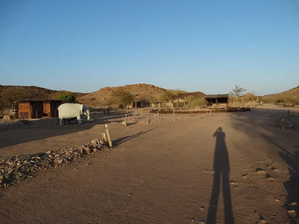 Paesaggio arido con strada sterrata e strutture rustiche nel deserto africano.