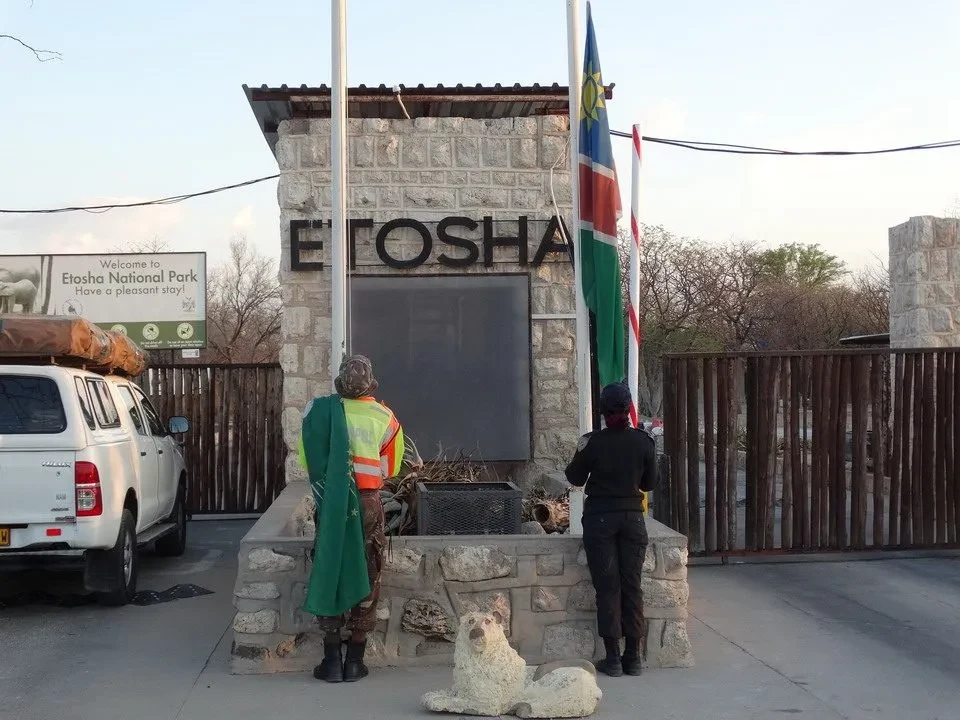 Ingresso al Parco Nazionale di Etosha in Namibia con bandiere e persone in primo piano.